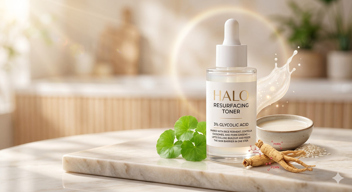 Renew Exfoliating Toner bottle on a marble surface with centella leaves and ginseng root